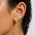 Close-up of an ear wearing a gold earring with water droplets on skin and hair.