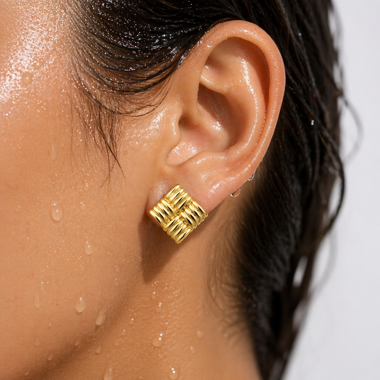 Close-up of an ear wearing a gold earring with water droplets on skin and hair.