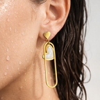 Gold-tone geometric heart drop earrings with pearlescent inlay, close-up on-ear shot