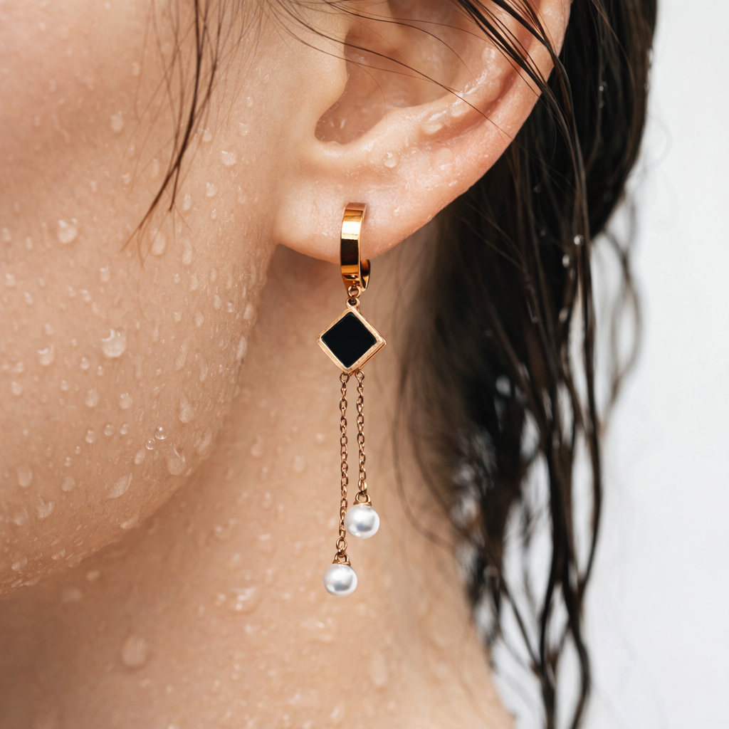 Close-up of an ear wearing a gold earring with a black gem and pearl drop, on a blurred background.