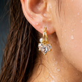 Gold heart-shaped earring with pearl detail worn by a person with wet skin.