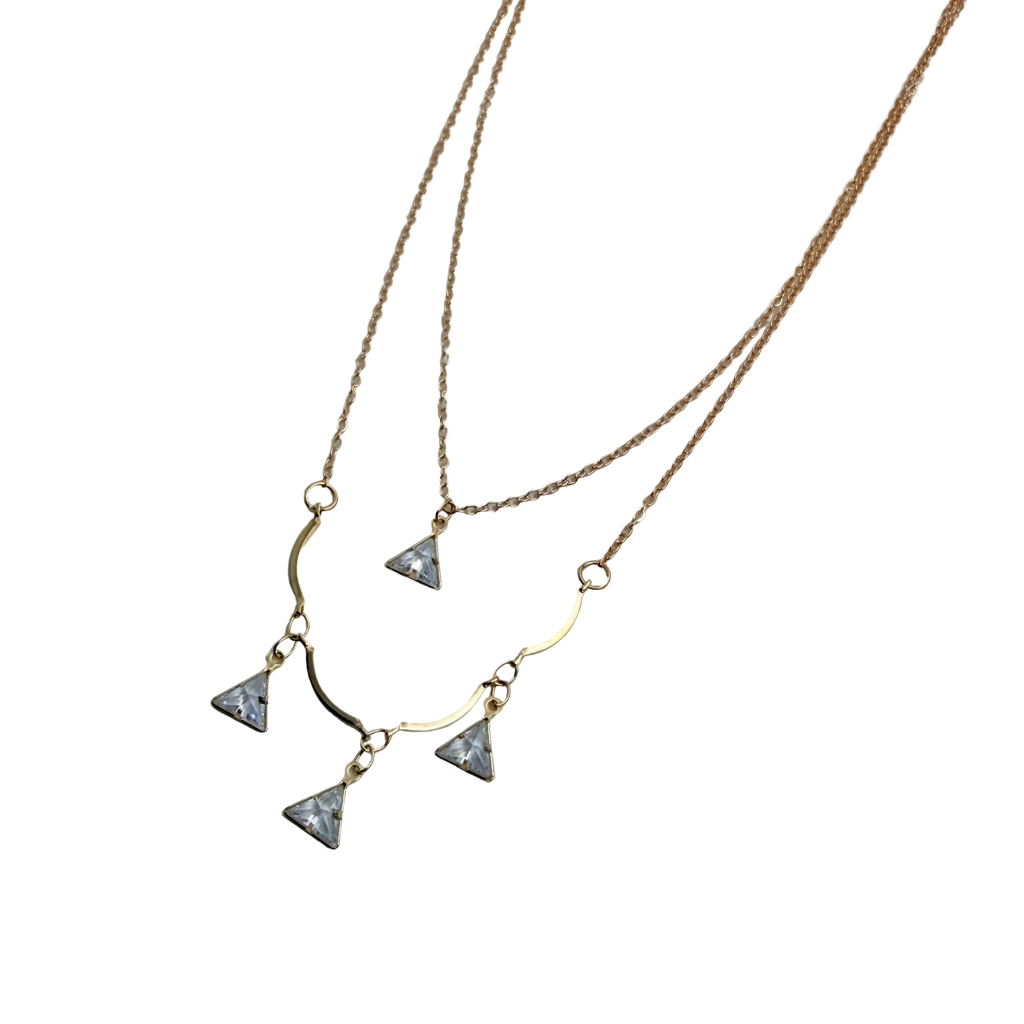 Gold-tone double-layered necklace with wavy bar and four trillion-cut crystal charms, flat lay on black background