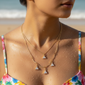 Gold-tone layered necklace with trillion-cut crystal charms, worn on model at the beach close-up