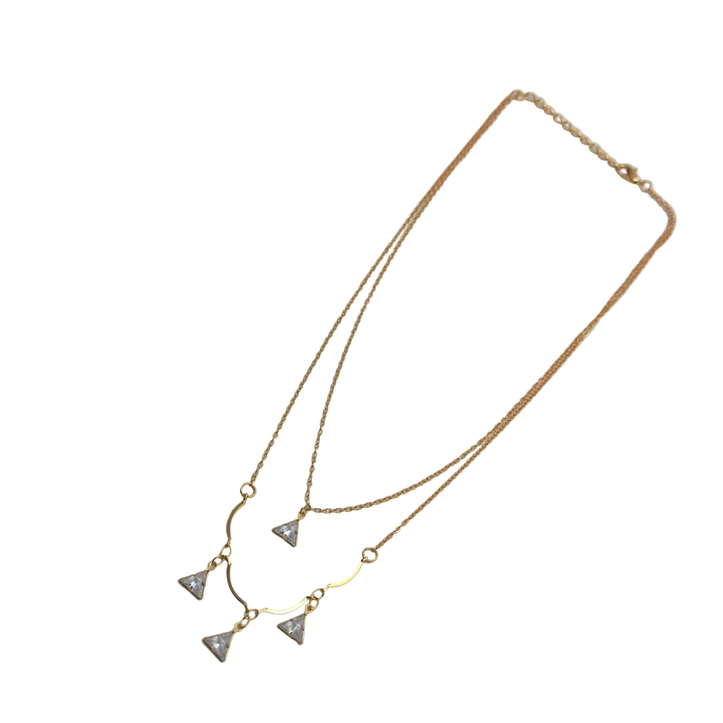 Gold-tone double-layered necklace with wavy bar and four trillion-cut crystal charms, angled flat lay on black background
