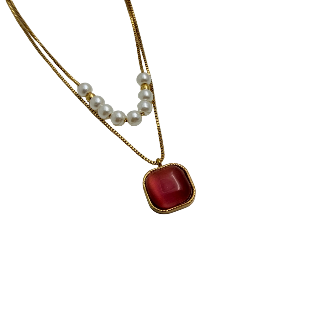 Gold-tone layered necklace with pearls and carnelian pendant, angled flat-lay view on black background