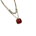 Gold-tone layered necklace with pearls and carnelian pendant, angled flat-lay view on black background