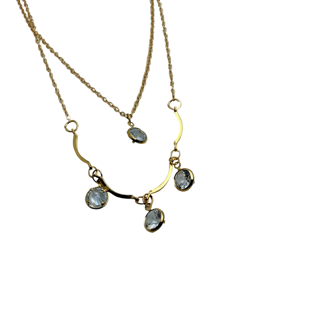 Gold-tone double-layer necklace with wavy bar and four clear crystal charms, flat lay close-up