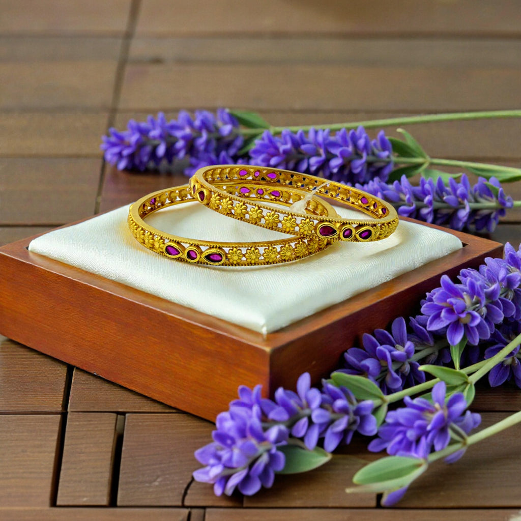 Gold studded bangles pair with pink stones and floral filigree, flat-lay with lavender flowers