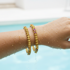Gold studded bangles with pink stones and floral filigree, worn on a wet wrist at poolside