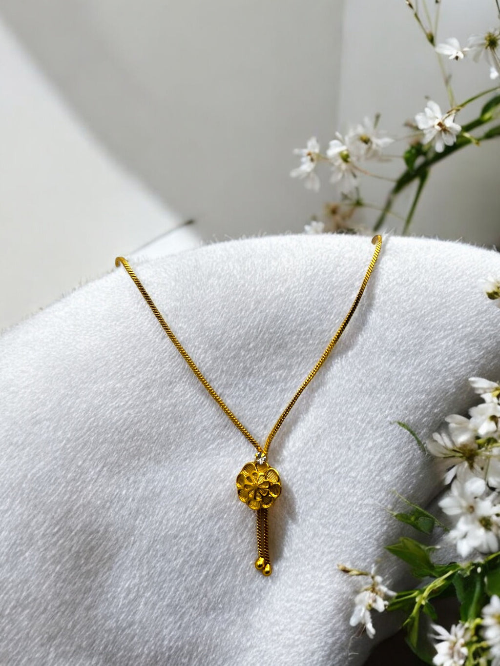 Gold floral pendant necklace with dangling bead accents, shown on a model wearing a saree