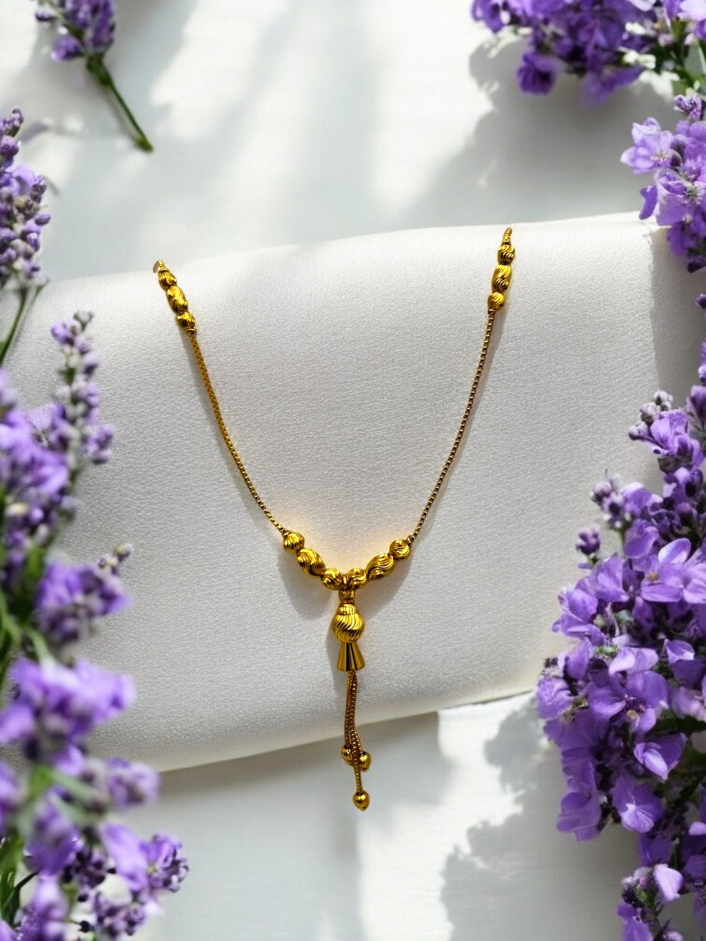 Gold-plated beaded tassel necklace with textured bead-cluster pendant, worn on model over a maroon and gold silk saree