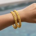 Gold filigree bangle set with engraved cutwork and black enamel accents, shown on wrist close-up
