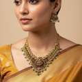 Antique gold temple necklace set with Goddess Lakshmi motif, worn on neck and ear showing peacock filigree and emerald green stone drops