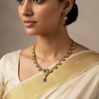Gold-toned floral necklace set with green, white and ruby-look CZ stones and peacock motif, flat-lay on white with petals