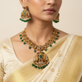 Antique gold-toned temple necklace set with peacock motifs and green bead drops, worn on model with saree