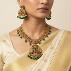 Antique gold-toned temple necklace set with peacock motifs and green bead drops, worn on model with saree