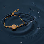 Adjustable chain slider bracelet with pave-stone disc centrepiece and floral accents, shown on a wet wrist by water