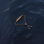 Rose gold-toned adjustable chain bracelet with triple halo stone motif, flat-lay on dark water
