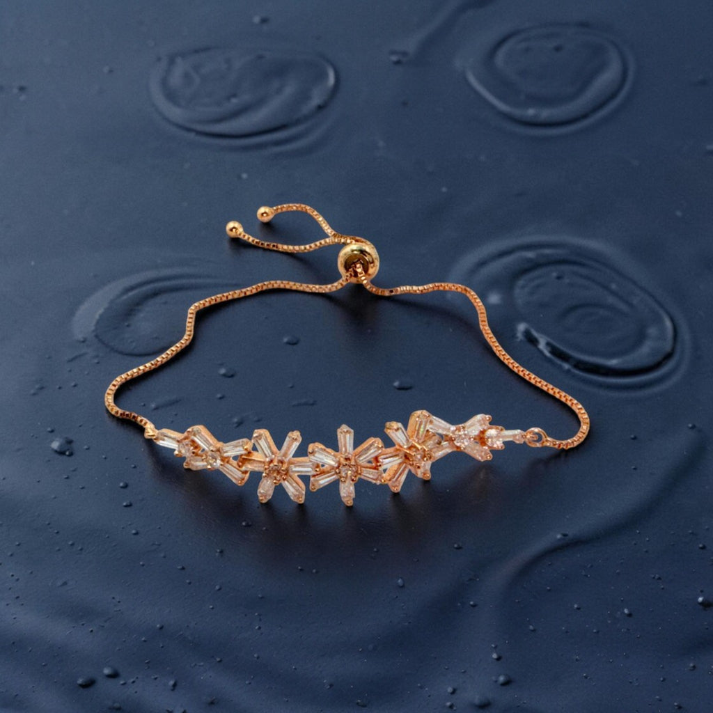 Rose gold-toned chain bracelet with baguette starburst clusters, worn on wrist with water droplets