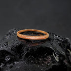 Rose gold crystal bangle bracelet with a pave sparkle bar, flat-lay close-up on a black rock