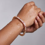 Rose gold crystal bangle bracelet with ruby-toned accents, worn on wrist under water droplets