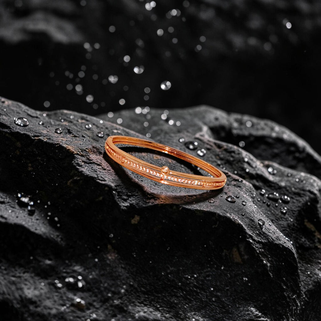 Rose gold bangle bracelet with pavé crystal line and pearl accent, flat-lay on dark stone