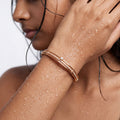 Rose gold bangle bracelet with pavé crystals and pearl accent, worn on wrist by model