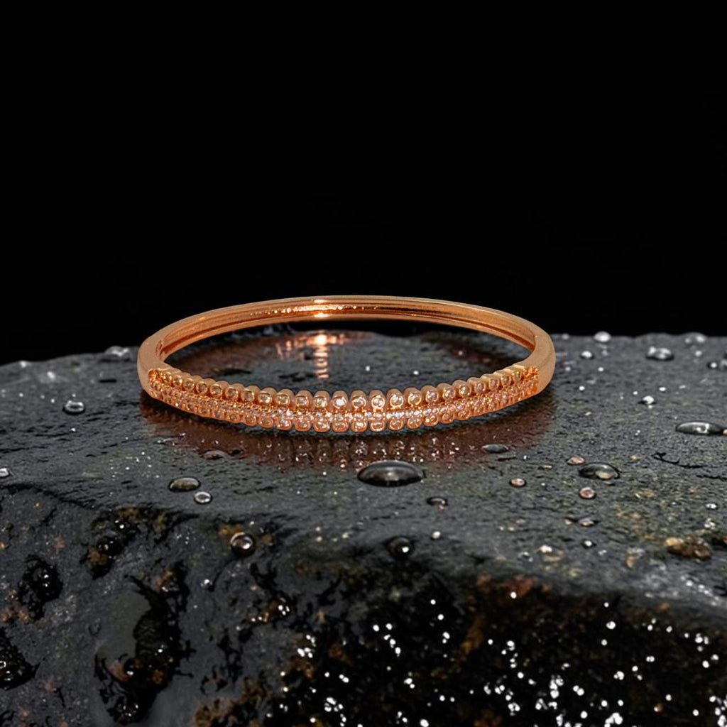 Rose gold crystal bangle bracelet with hinged clasp, flat-lay on dark wet stone