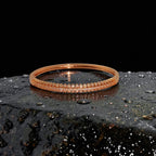 Rose gold crystal bangle bracelet with hinged clasp, flat-lay on dark wet stone