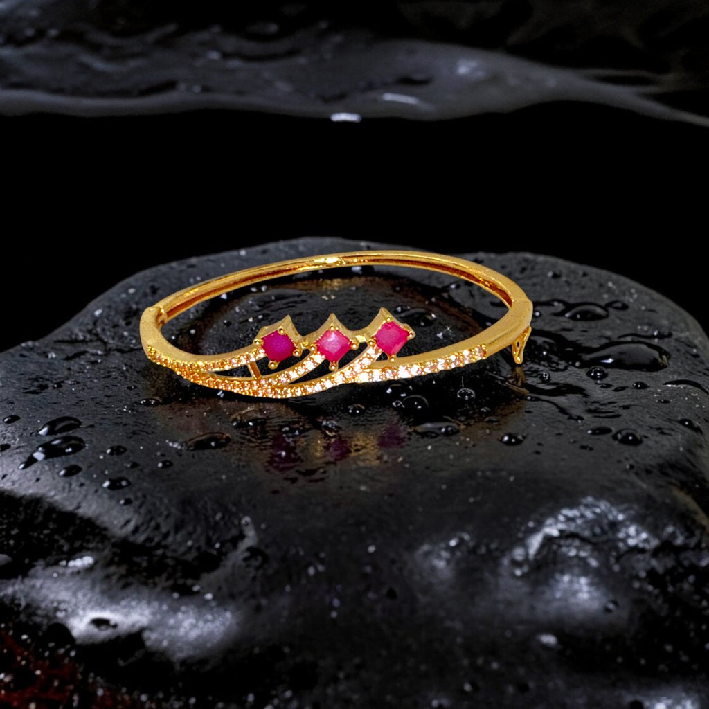Gold plated bracelet with red gemstones on a black, water-textured surface