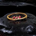 Gold plated bracelet with red gemstones on a black, water-textured surface