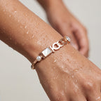 Rose gold-tone link charm bangle bracelet with pearl and crystal accents, worn on wet wrist close-up
