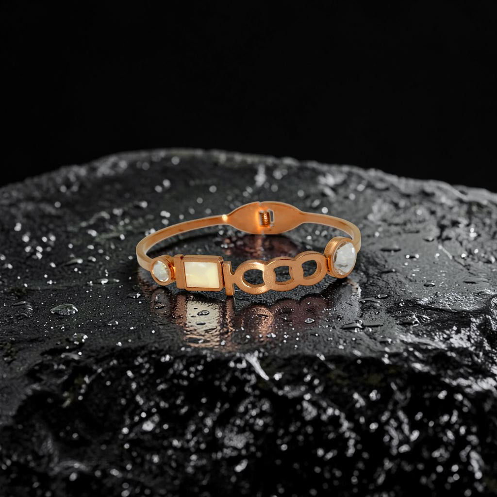 Rose gold-tone link charm bangle bracelet with mother-of-pearl centerpiece and crystal accents, flat-lay on dark stone