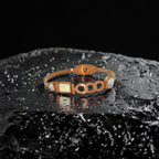 Rose gold-tone link charm bangle bracelet with mother-of-pearl centerpiece and crystal accents, flat-lay on dark stone