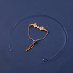 Rose gold butterfly bracelet with CZ stones and pearl accents, flat-lay shot on dark surface with water droplets