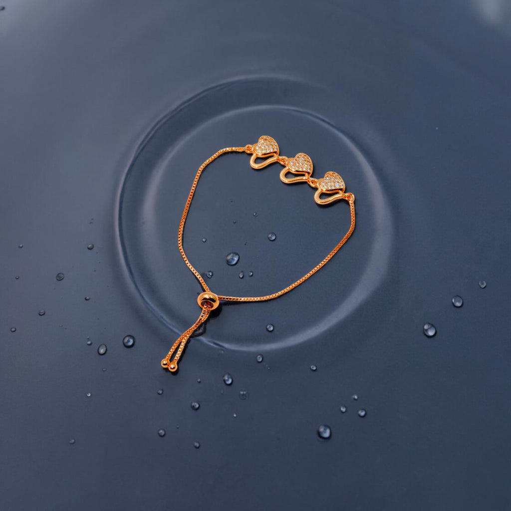 Rose gold triple heart bracelet with crystal-pave hearts and adjustable slider chain, flat-lay on water