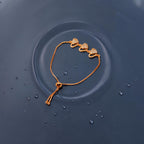 Rose gold triple heart bracelet with crystal-pave hearts and adjustable slider chain, flat-lay on water