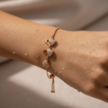 Rose gold triple heart bracelet with crystal-pave hearts and adjustable slider chain, flat-lay on water