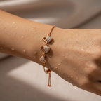 Rose gold triple heart bracelet with crystal-pave hearts and adjustable slider chain, flat-lay on water