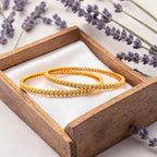 Gold crystal-studded bangle set worn on wrist, close-up with water droplets showing waterproof finish