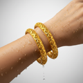 Carved gold-plated bangles with floral openwork design, worn on wrist showing waterproof water droplets