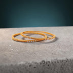 Gold twisted bangle pair with CZ stone detailing, flat-lay on stone surface