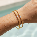 Gold twisted bangles with CZ stone detailing worn on wrist, waterproof finish shown wet