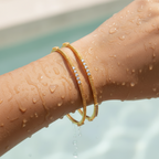 Gold twisted bangles with CZ stone detailing worn on wrist, waterproof finish shown wet