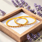 Gold bezel-set crystal bangles stacked on wrist, wet-look shot showing waterproof shine