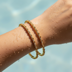 Gold bezel-set crystal bangles stacked on wrist, wet-look shot showing waterproof shine