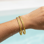 Gold cutwork textured bangles stacked on wrist, water droplets showing waterproof finish