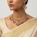 Woman wearing a gold and pink necklace and earrings with a beige saree.