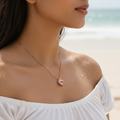 Rose gold crystal open heart pendant necklace, worn on model at neckline, close-up beach shot