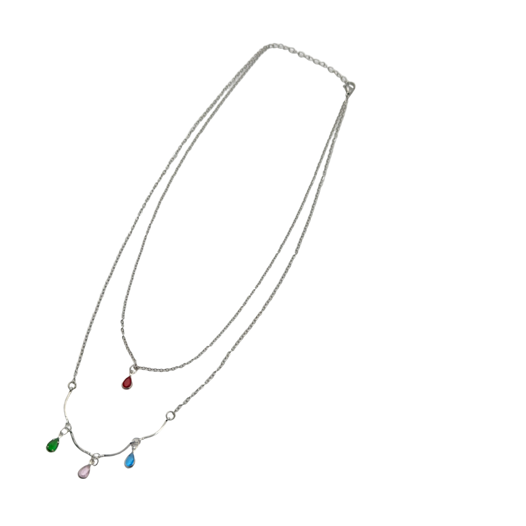 Silver-tone double-layer necklace with ruby, emerald, blue and pink teardrop crystal charms, flat-lay on black background